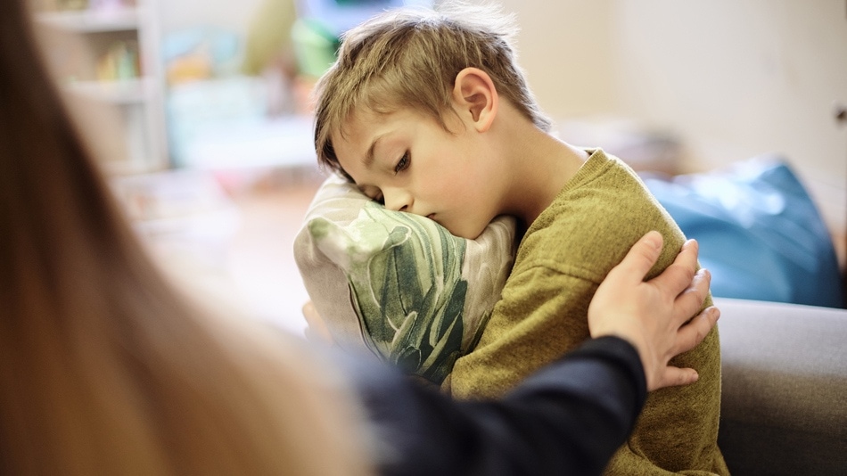 Niño que ha sufrido bullying abrazando una almohada es consolando por el brazo de una psicóloga
